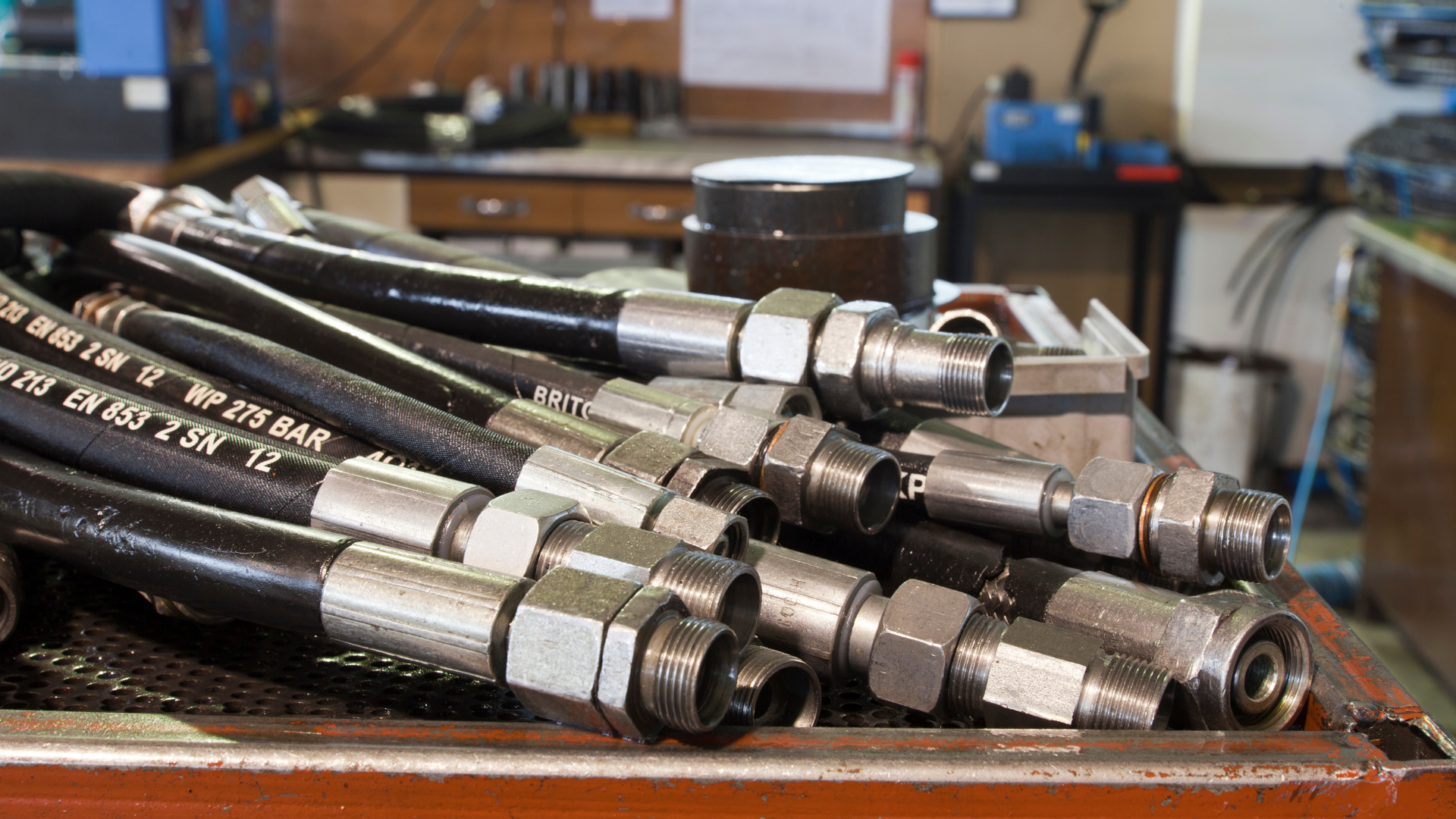 Coiled black hydraulic hoses with silver metal fittings on a workbench in a workshop