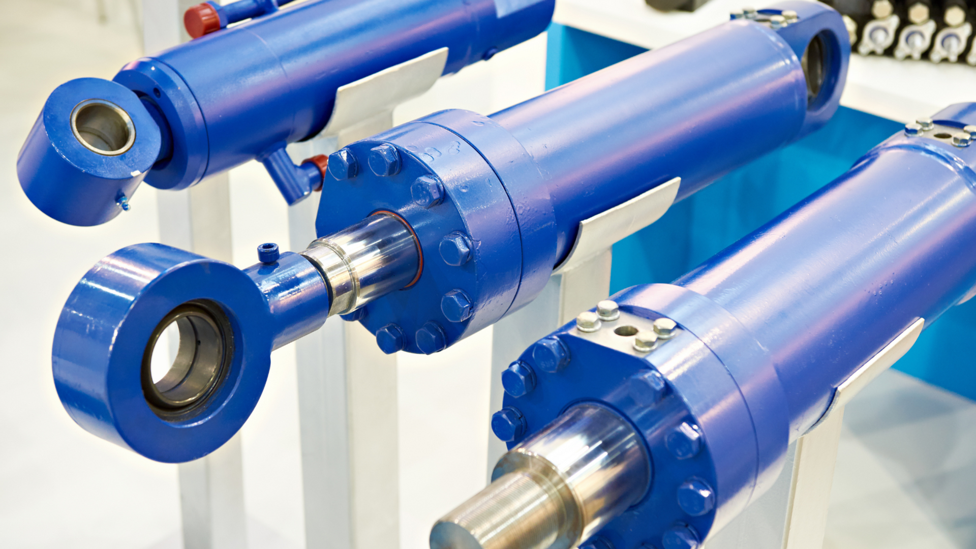 Blue hydraulic cylinders with chrome rods displayed on a white stand in a showroom