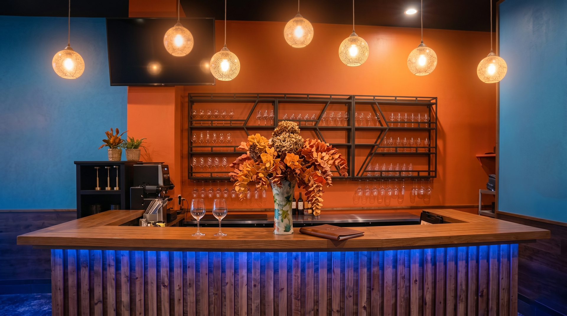 Cozy bar counter with hanging lights, blue and orange walls, and a vase of flowers on the counter