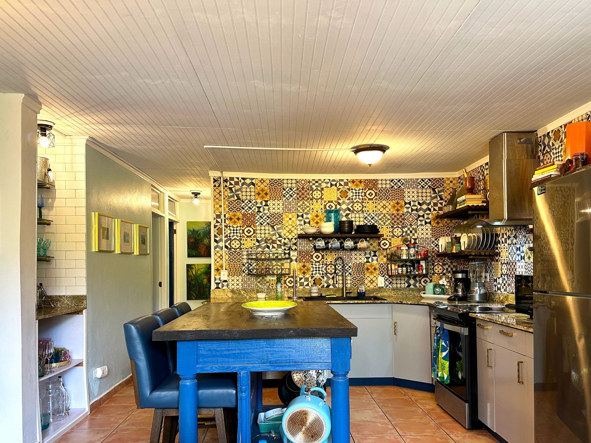 Bright kitchen with patterned backsplash, dark island, blue stools, and stainless steel appliances, located near El Yunque