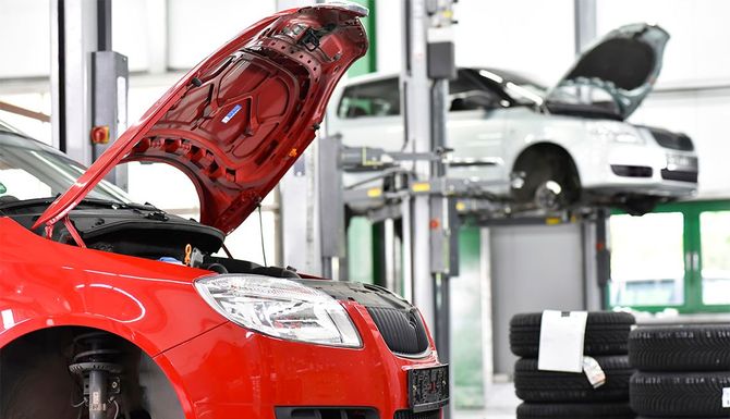 Red car with open hood in auto repair shop, white car lifted on a hoist in the background