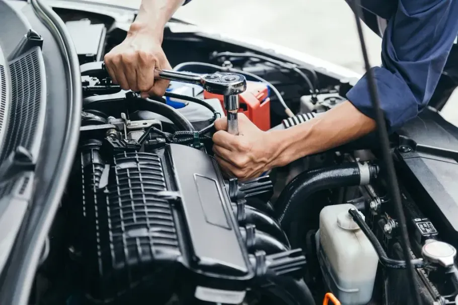 Mechanic working under a car hood, tightening engine components with tools in a garage