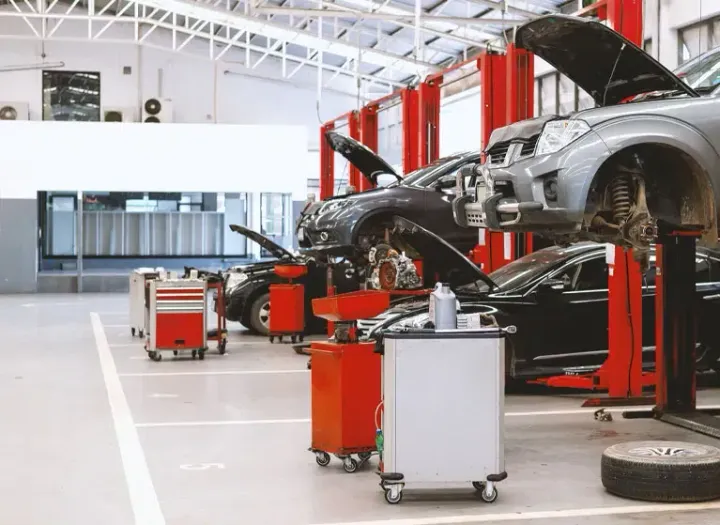 Car workshop with several cars lifted on red hydraulic lifts and repair equipment on the floor