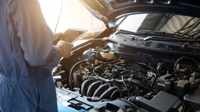 Person inspecting an open car engine in bright sunlight