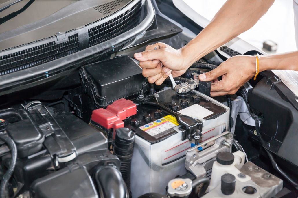 Hands working on a car battery in an open engine bay, with jumper cables attached.
