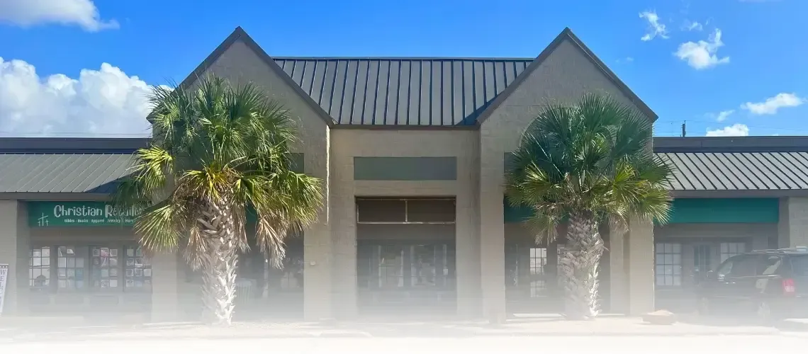 A light-colored building with a central entrance and palm trees on either side under a blue sky.