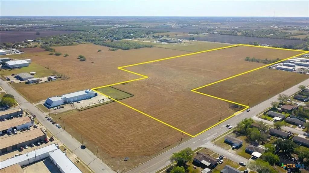 Aerial view of a large, vacant lot outlined in yellow, bordered by roads and buildings in an urban area.