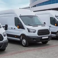 White vans parked in front of a building with a curved glass facade.