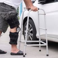 Man using a walker near a car, wearing a leg brace.