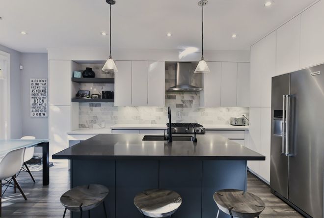 A kitchen with a large island , stools , a refrigerator and a stove.