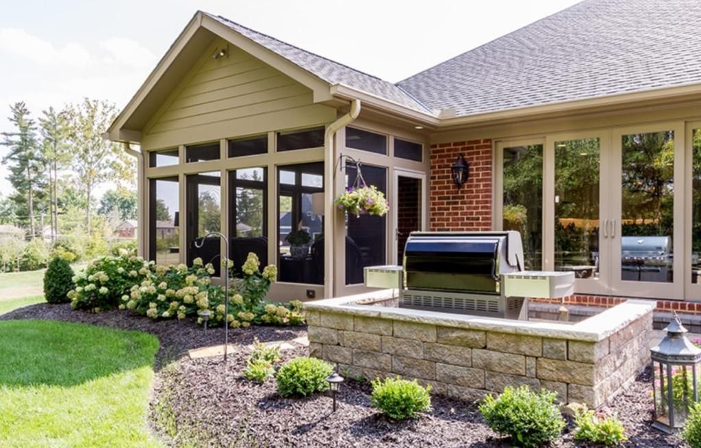 A house with a screened in porch and a grill in the backyard.