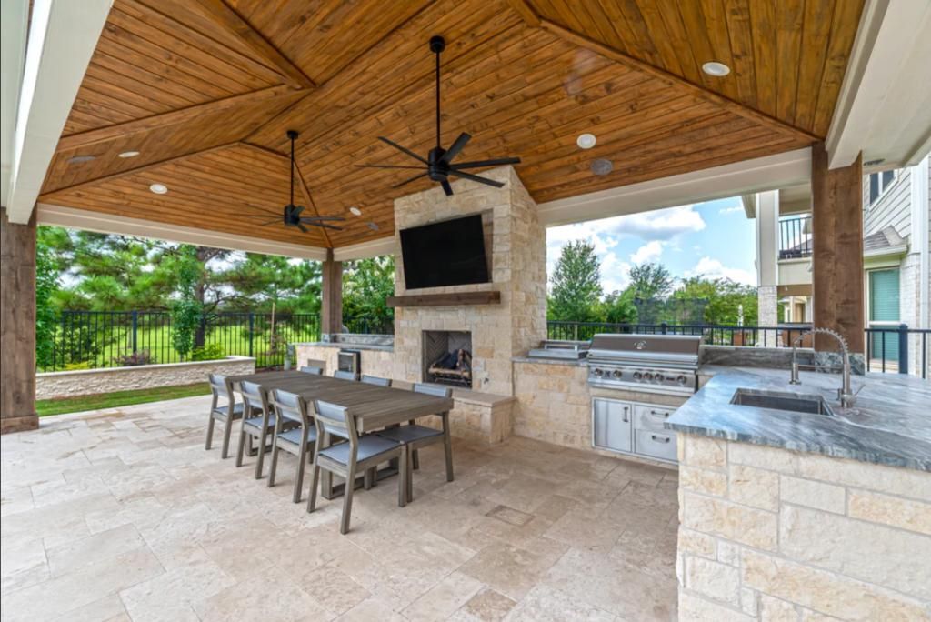 A covered patio with a table and chairs and a fireplace.