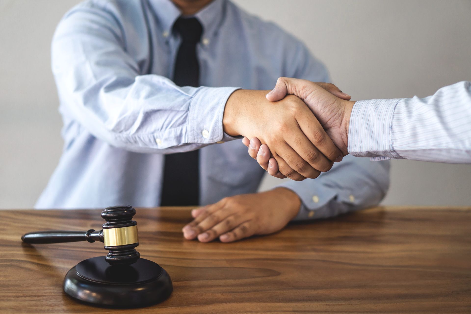 Business handshake over a wooden desk with a judge's gavel in the foreground