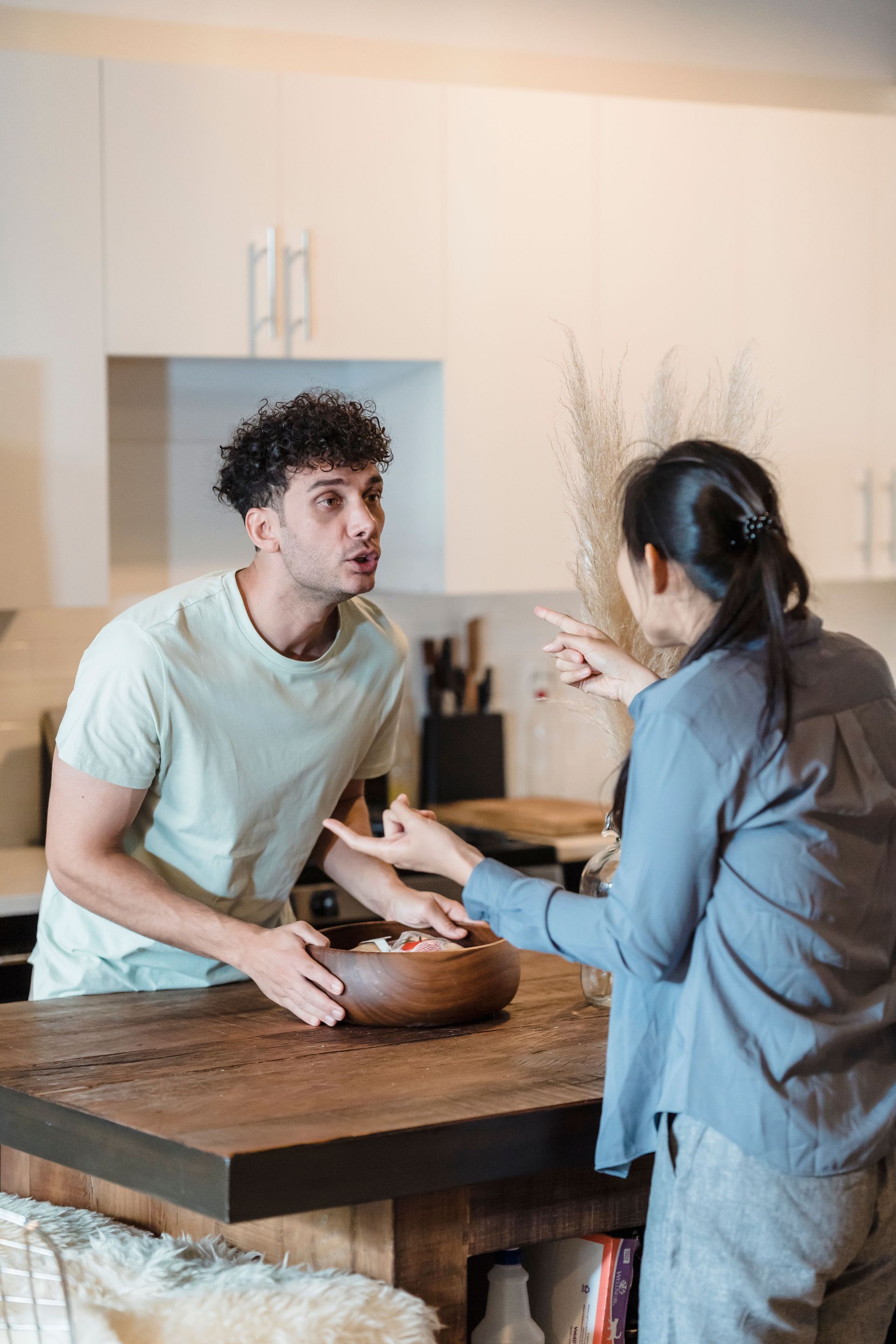 Two people talking across a kitchen island, one holding a bowl in a bright modern kitchen.