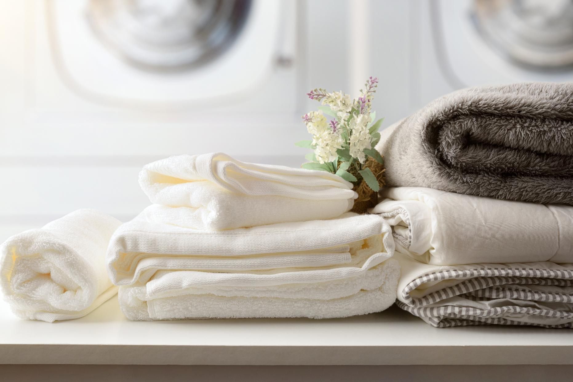 Stacked white towels with folded beige towels and small flowers on a bathroom counter
