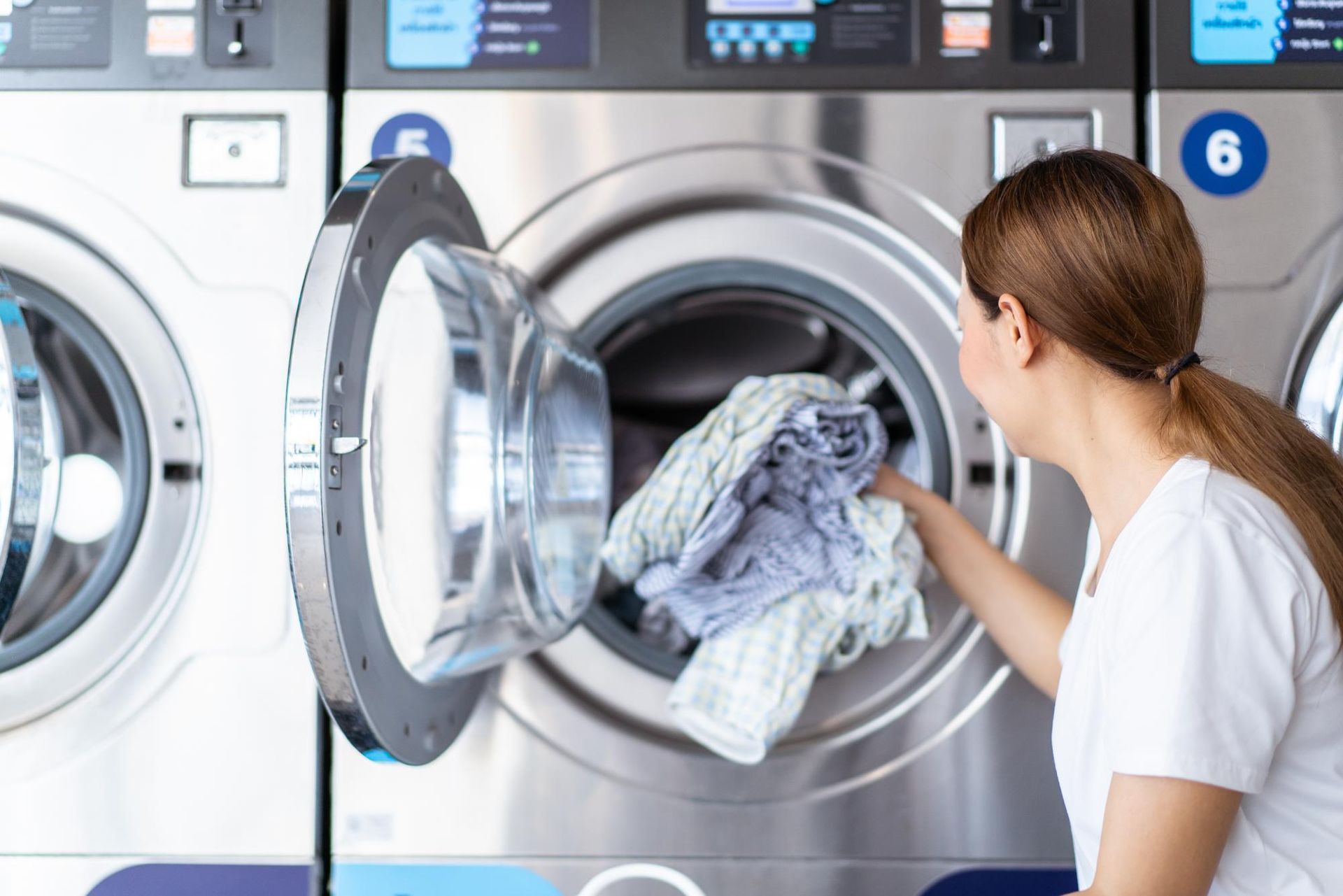 Woman loading clothes into a front-loading washing machine in a laundromat
