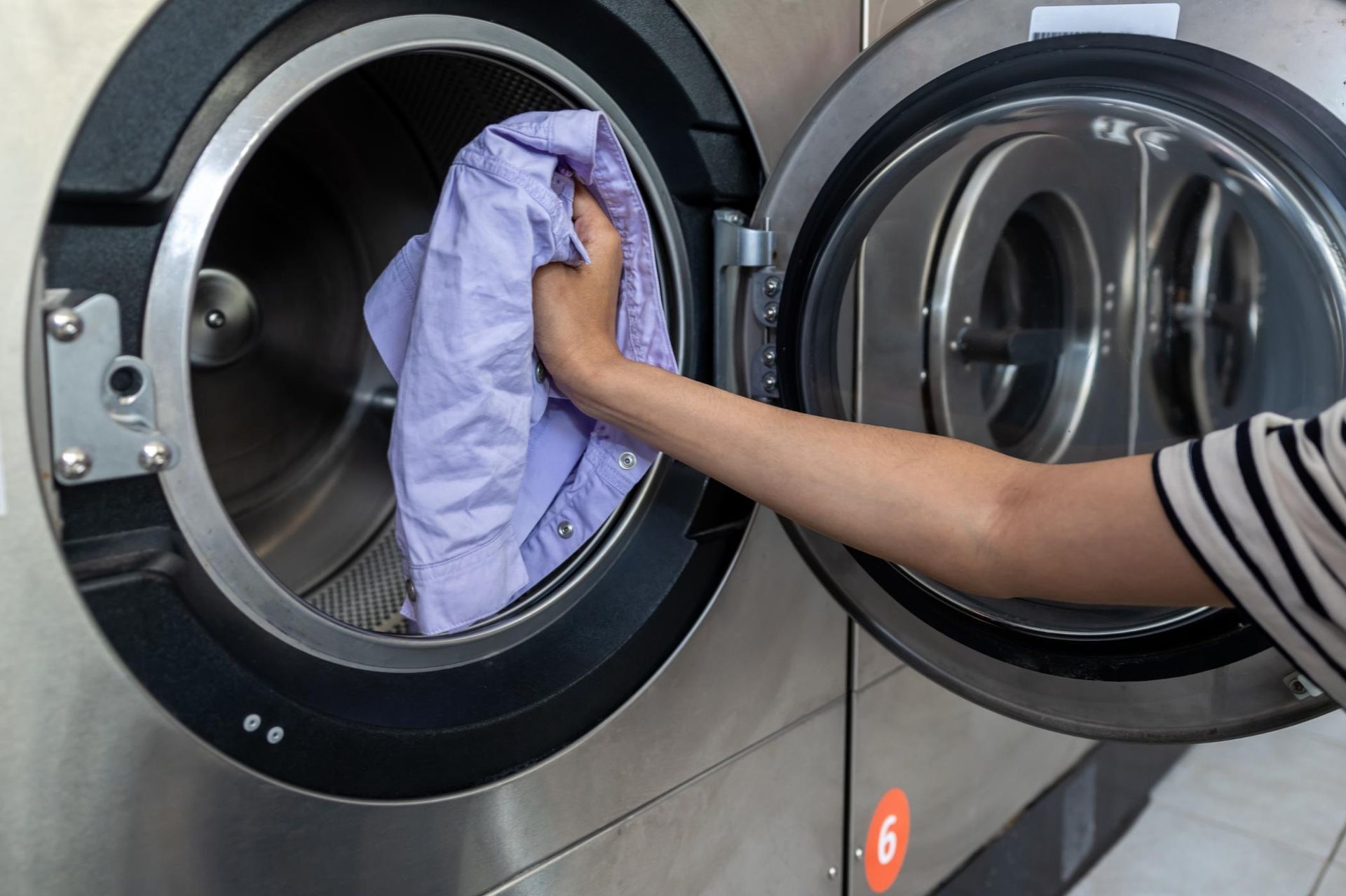 Arm in striped sleeve placing purple laundry into a front-loading washing machine