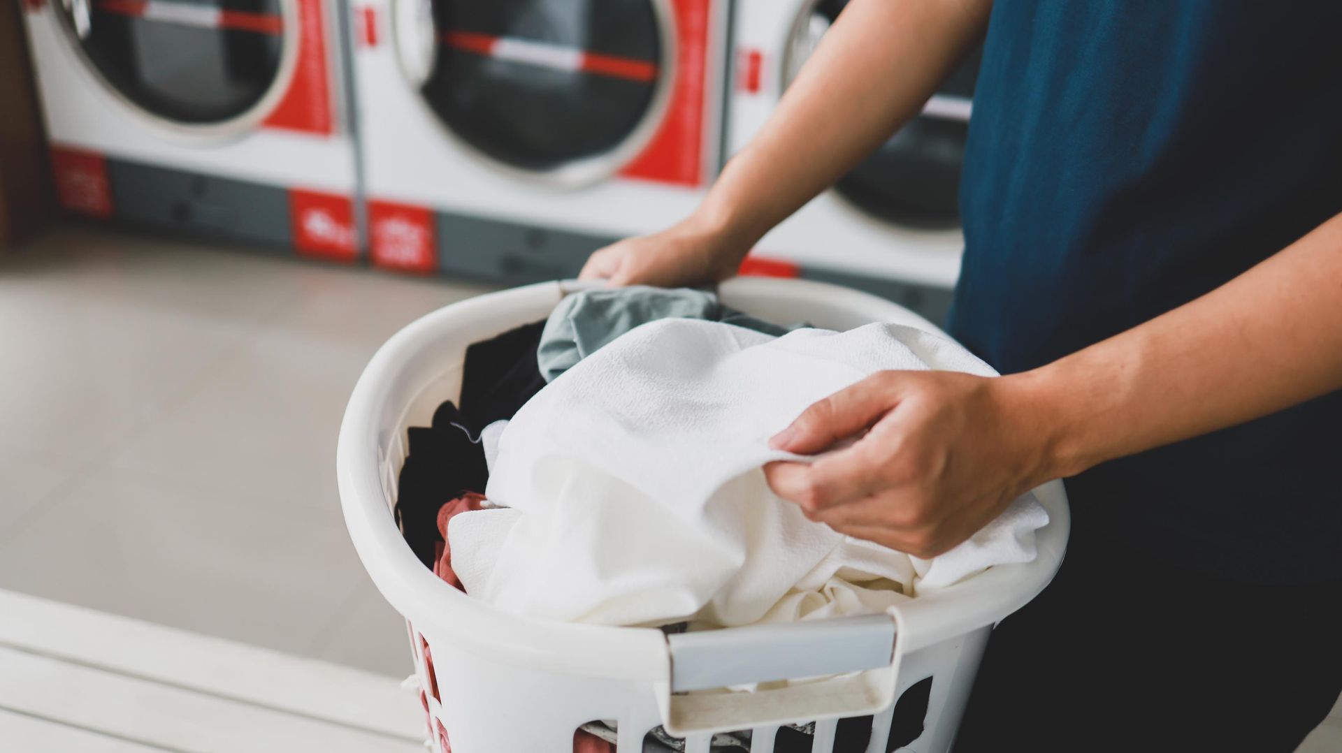 Person placing clothes into a laundry basket in a laundromat