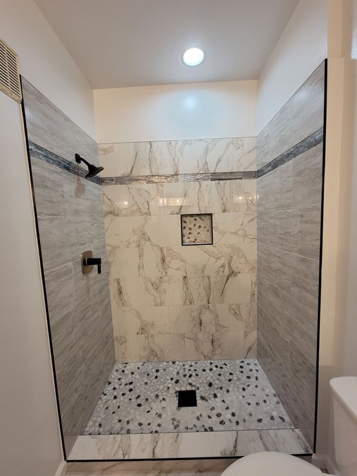 Newly tiled shower with black fixtures and pebble floor created by VA Creative Renovations