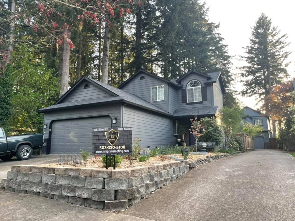 Gray house with a stone retaining wall, driveway, and trees in a wooded neighborhood