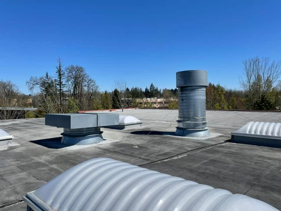 Rooftop with vents and a metal exhaust stack under a clear blue sky