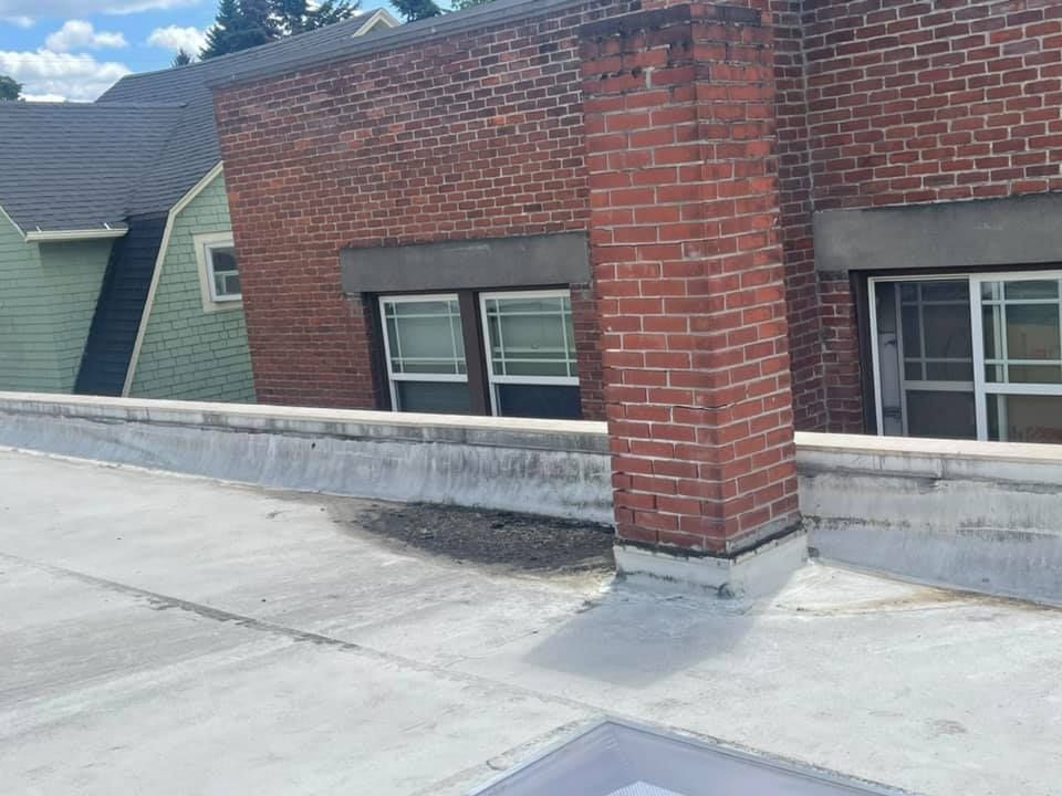 Flat rooftop with a red brick chimney and low concrete parapet in front of neighboring buildings.
