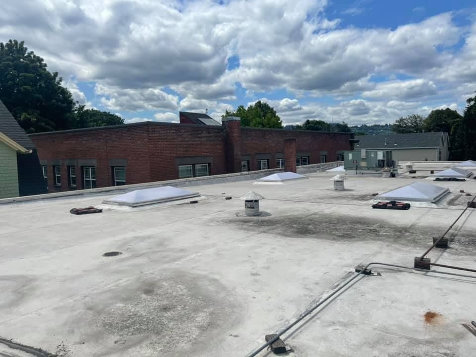 Flat rooftop with HVAC units beside a red brick building under a cloudy sky