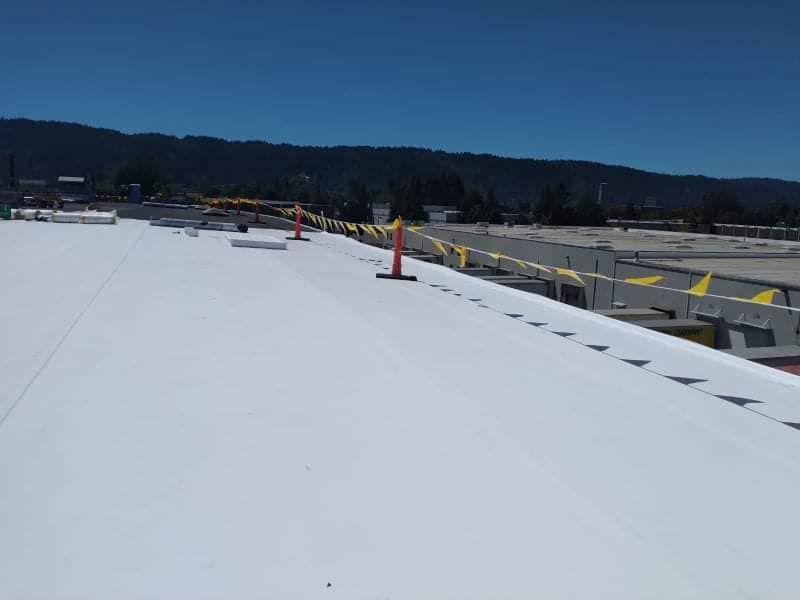 Large white rooftop with orange cones and yellow caution tape under a clear blue sky