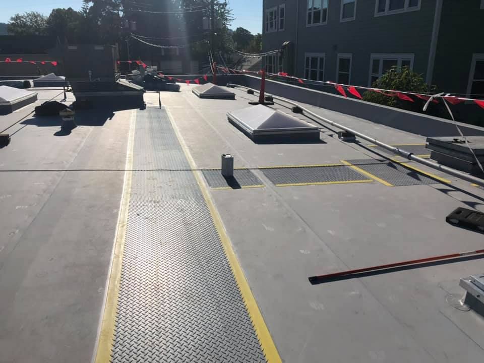 Flat rooftop with rooftop equipment, safety rails, and bright yellow walk lines in sunlight