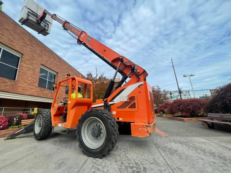 Orange telehandler with raised boom parked beside a brick building outdoors