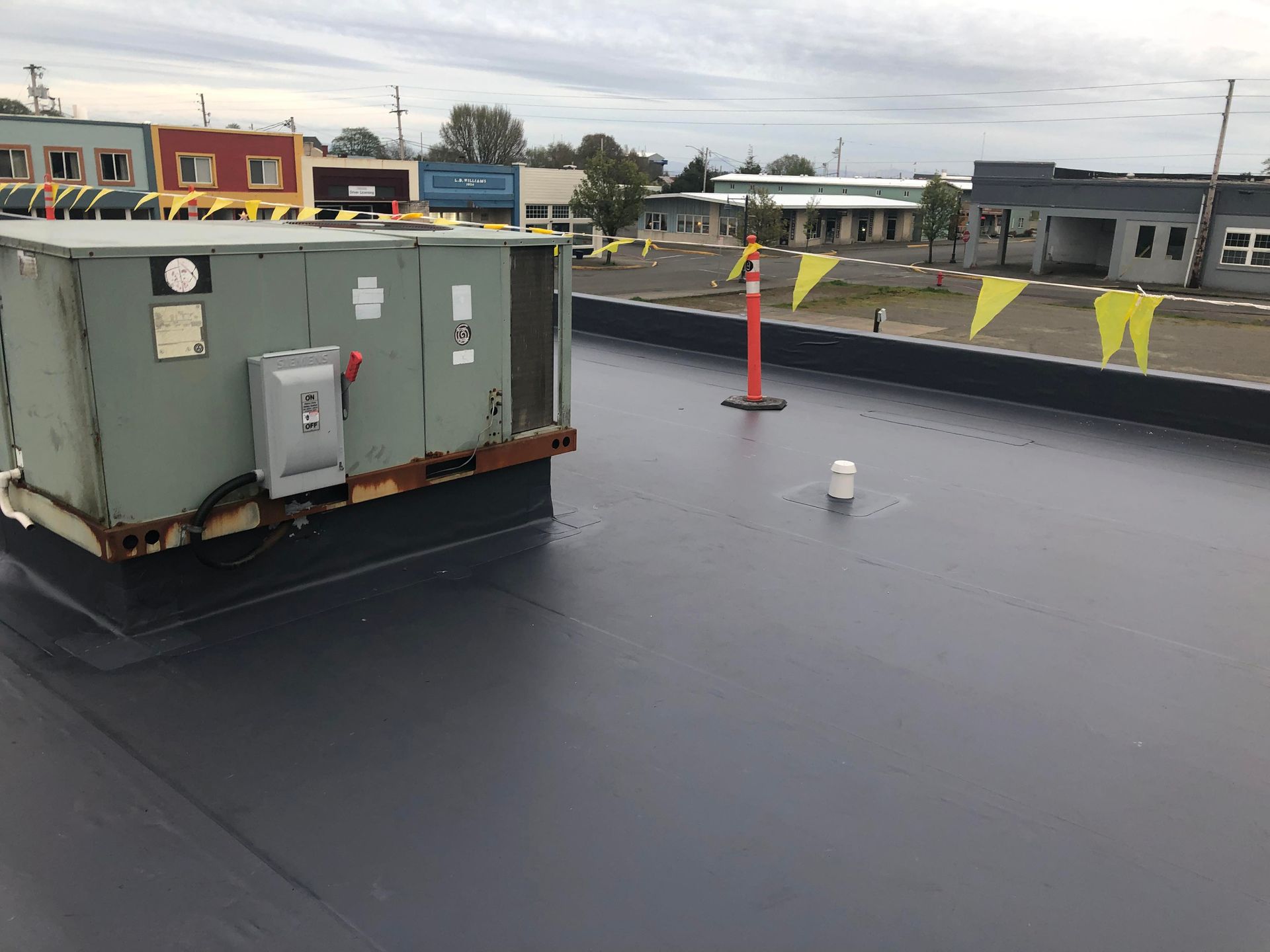 Rooftop with a large HVAC unit, safety cone, and yellow flags under an overcast sky.