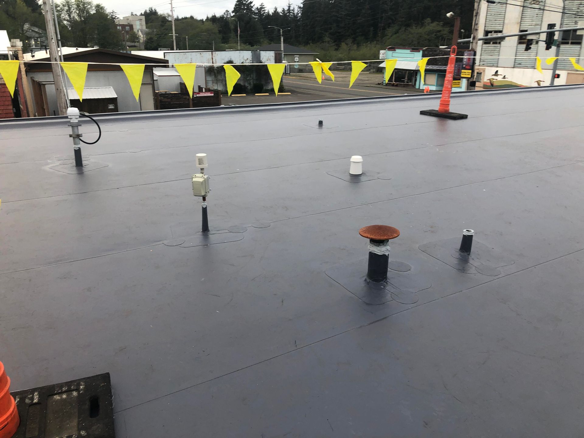 Wet rooftop with scattered pipes and safety cones beside a yellow-black barricade fence