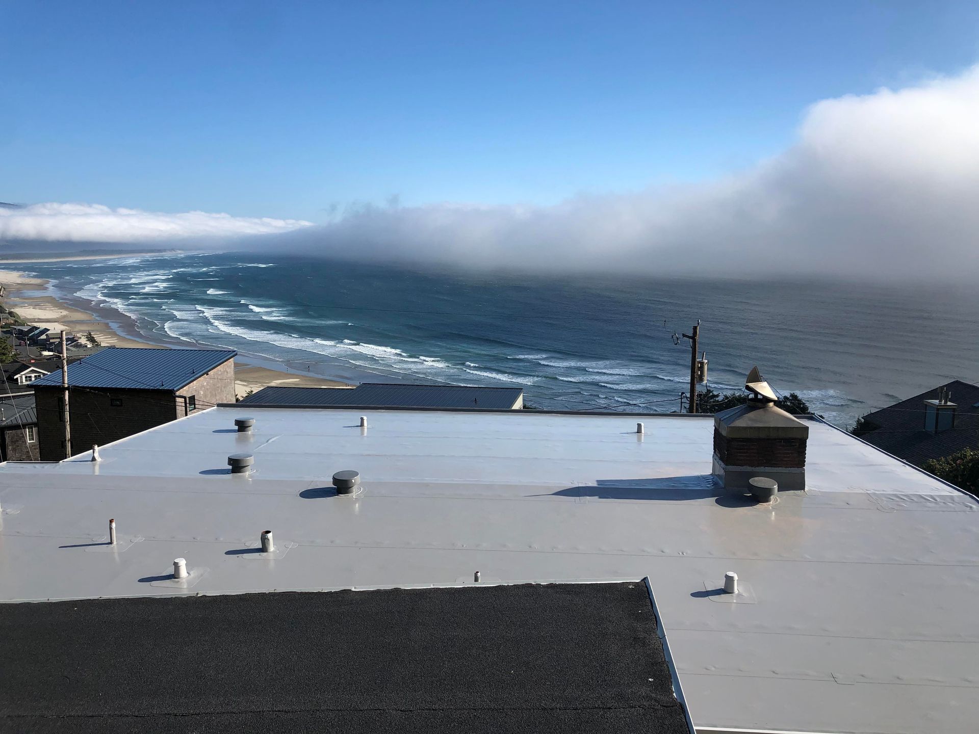 Commercial flat rooftop overlooking a cloudy ocean coastline with waves and a fog bank
