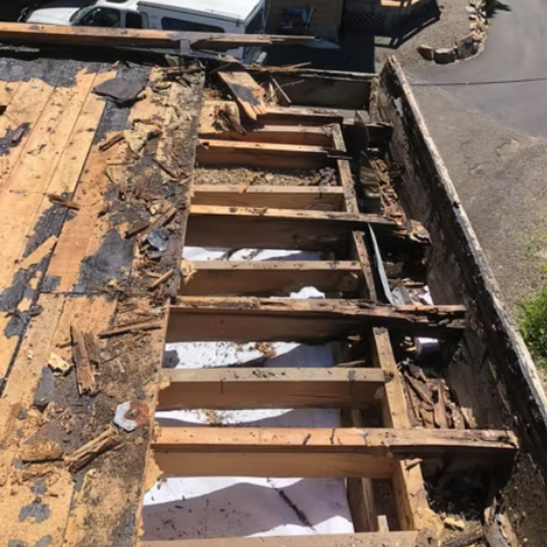 Exposed roof rafters and torn shingles beside a street, showing severe roof damage
