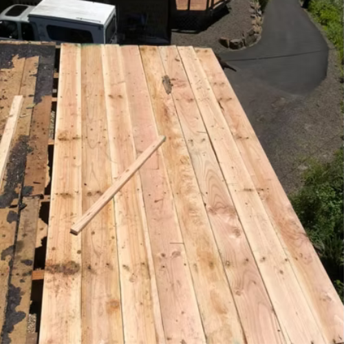 Stacked wooden planks on a roof beside a white van and driveway in sunlight