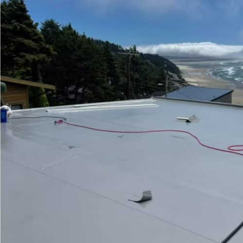 Flat white rooftop with red cord, overlooking pine trees, ocean waves, and a cloudy coastline.