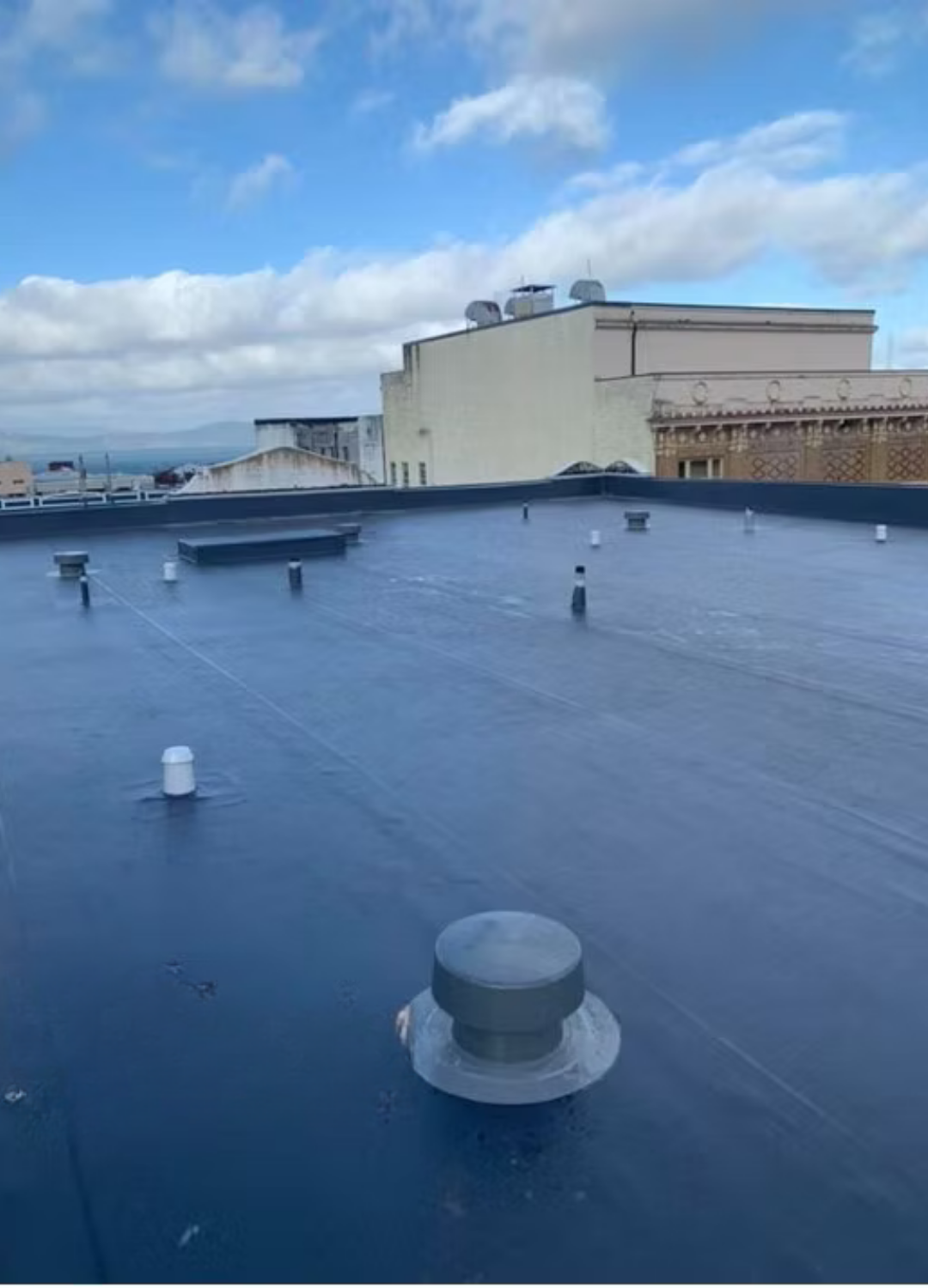 Flat rooftop with dark blue surface, vents, and a cloudy sky in the background