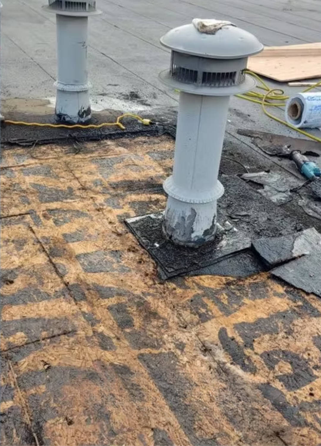 Roof with damaged shingles around two white vent pipes and exposed underlayment