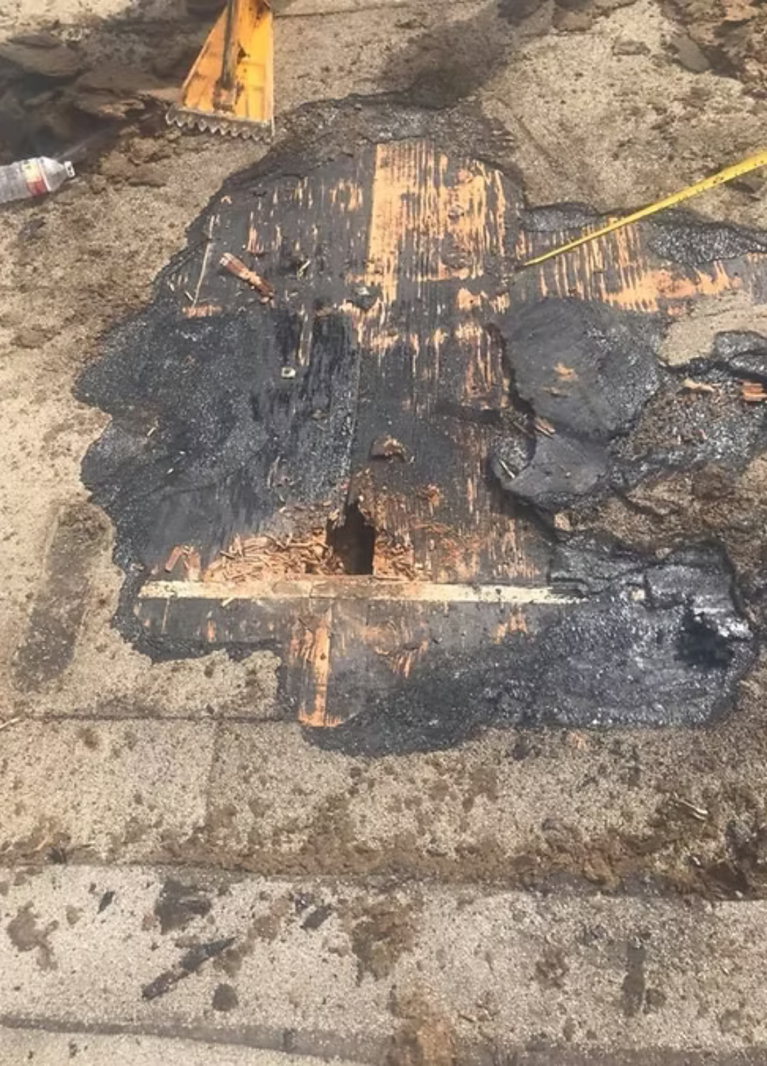 Charred burnt object on a concrete surface with black soot and orange scorch marks, near a yellow cord.