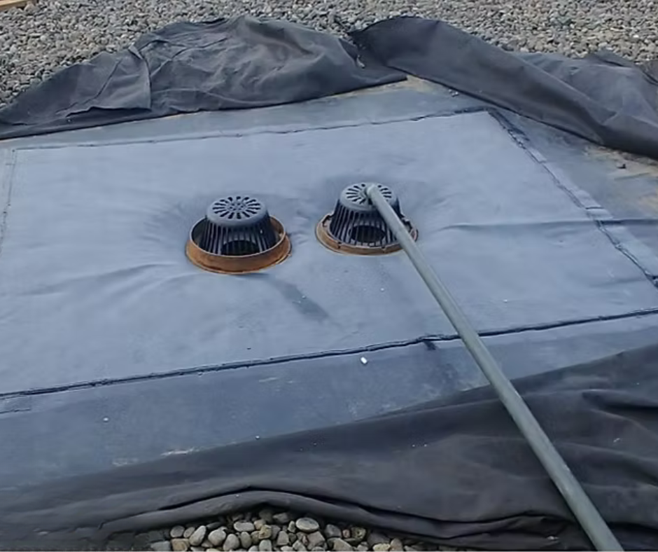 Covered rooftop with two circular vents and a hose on a gray tarp surface.