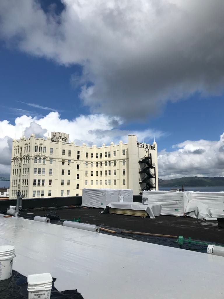 White rooftop with HVAC units and a cream-colored building under a cloudy blue sky.