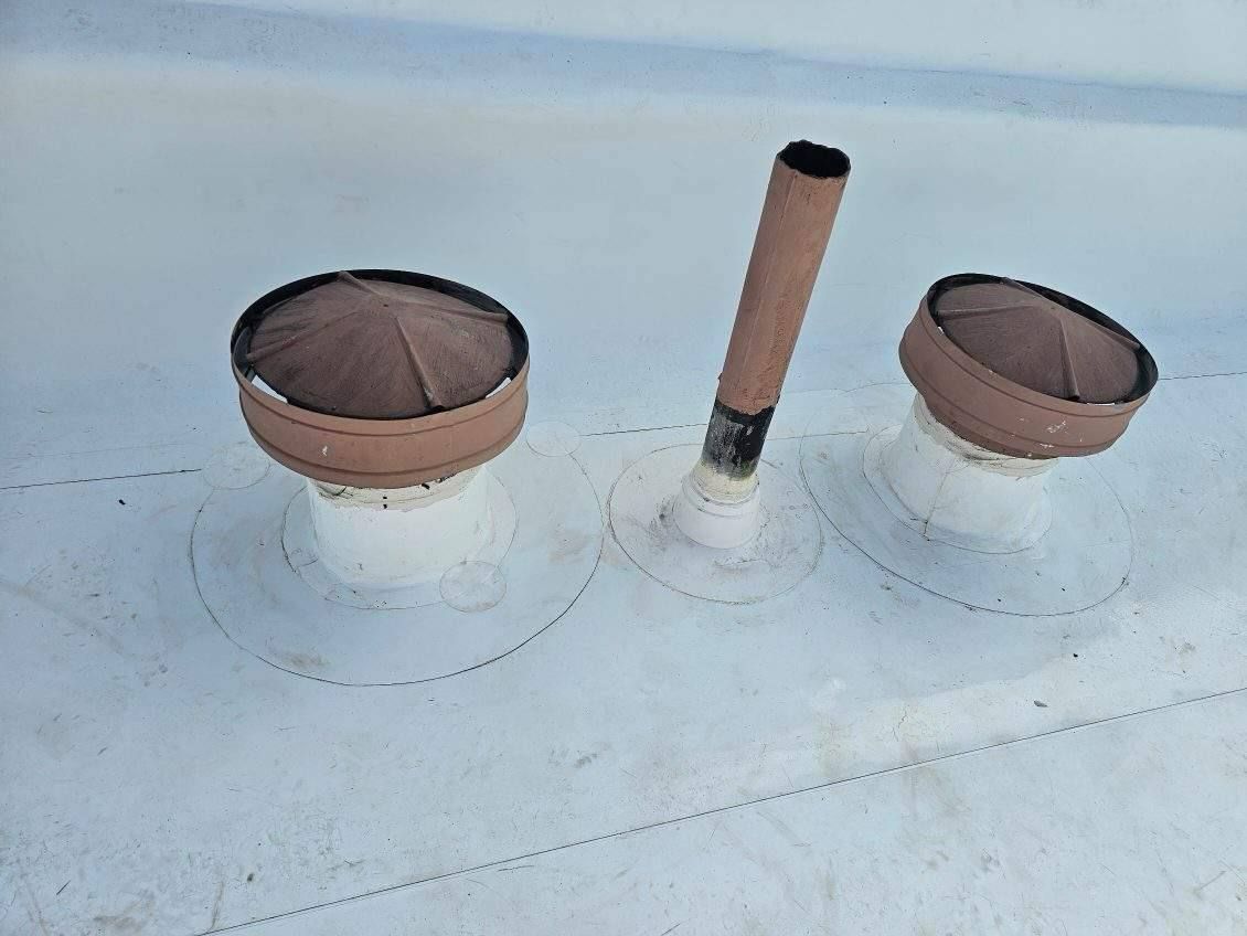 Two roof vents on a light blue metal roof, with a tan pipe between them.