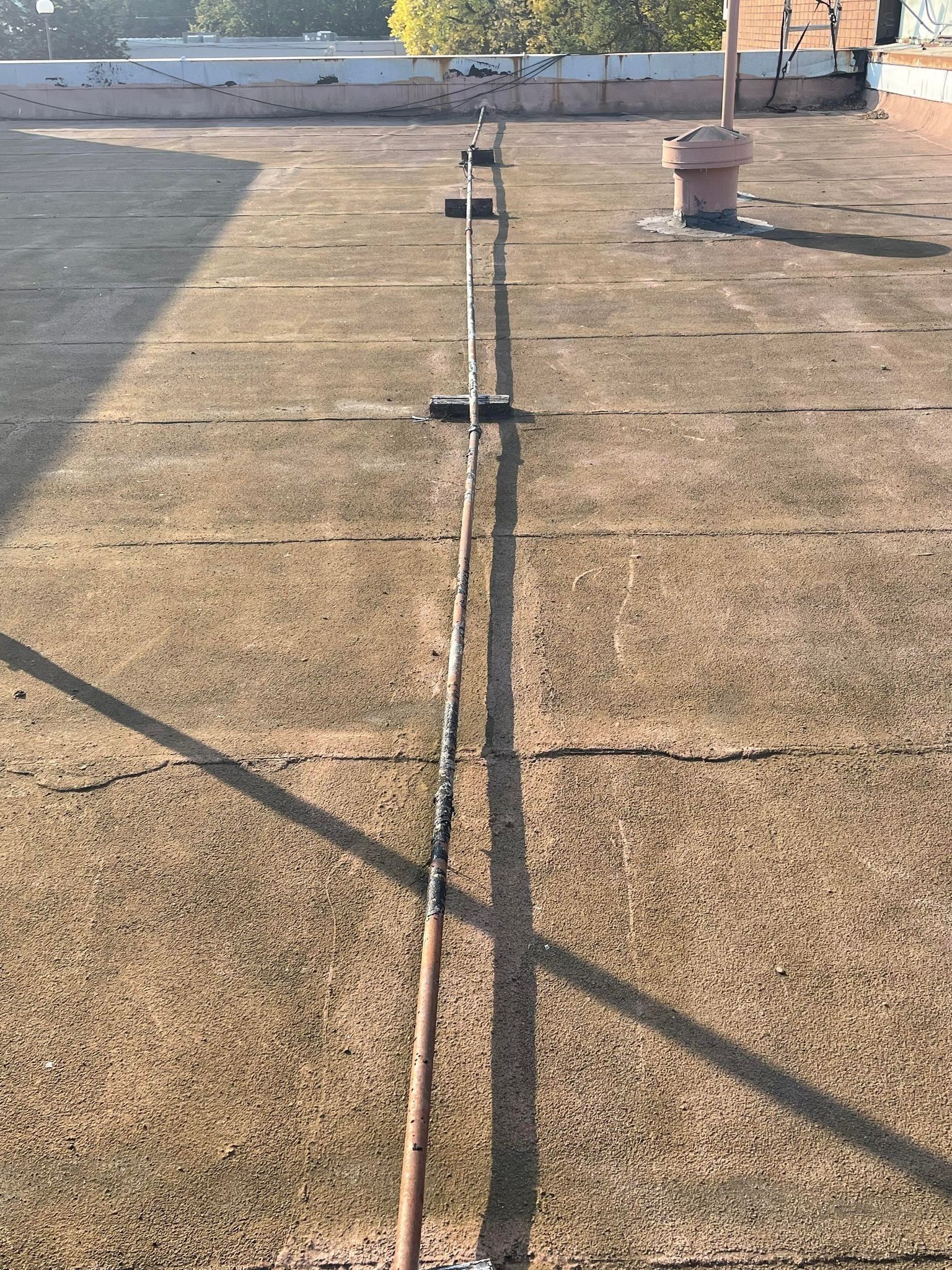 Long crack in a concrete rooftop or parking lot, with shadows and a small planter nearby.