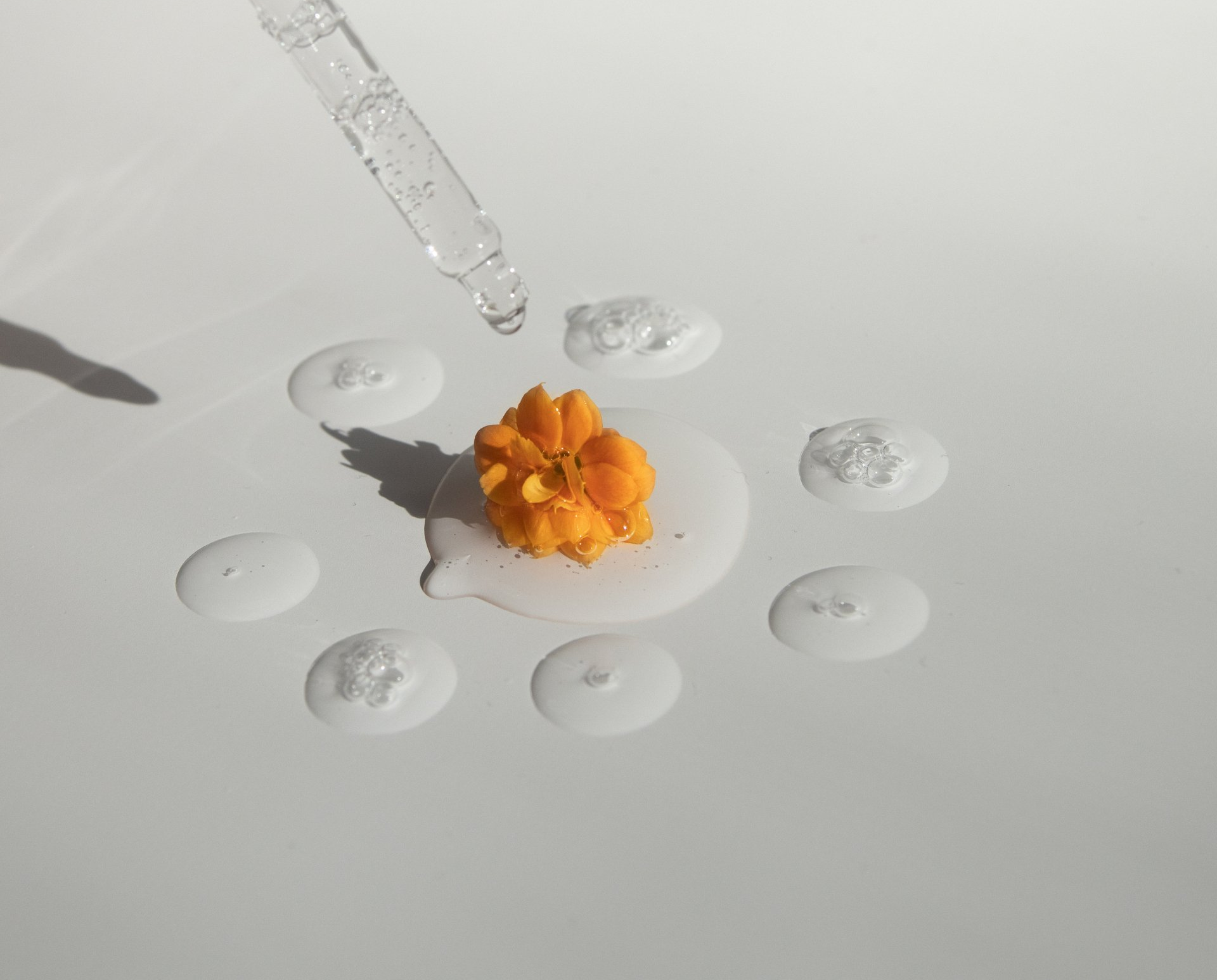 Dropper dispensing liquid onto a bright orange, textured substance surrounded by clear droplets on a white surface.