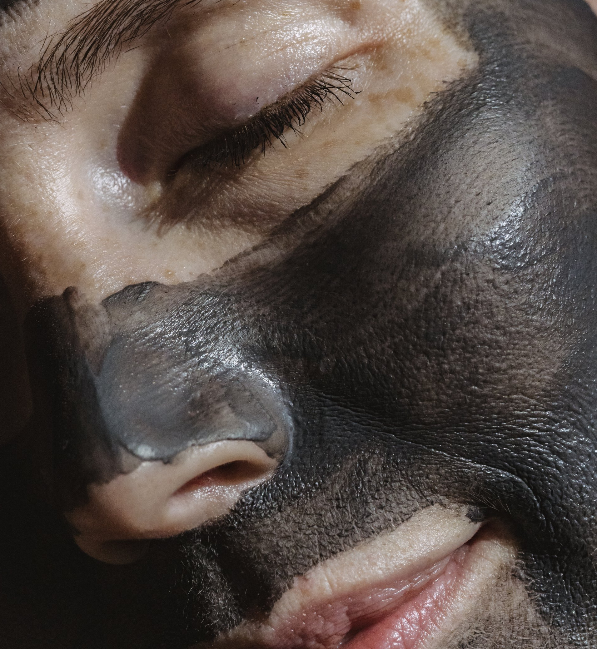 Face with dark charcoal mask, nose strip applied.