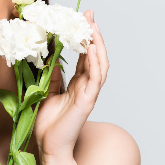 Eine Hand hält weiße Blumen, Nahaufnahme der Schulter und des Gesichts einer Person, heller Hintergrund.