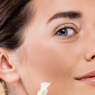 Frau mit heller Haut, grünen Augen und einem sanften Lächeln. Hält eine weiße Blume vor ihrem Gesicht.