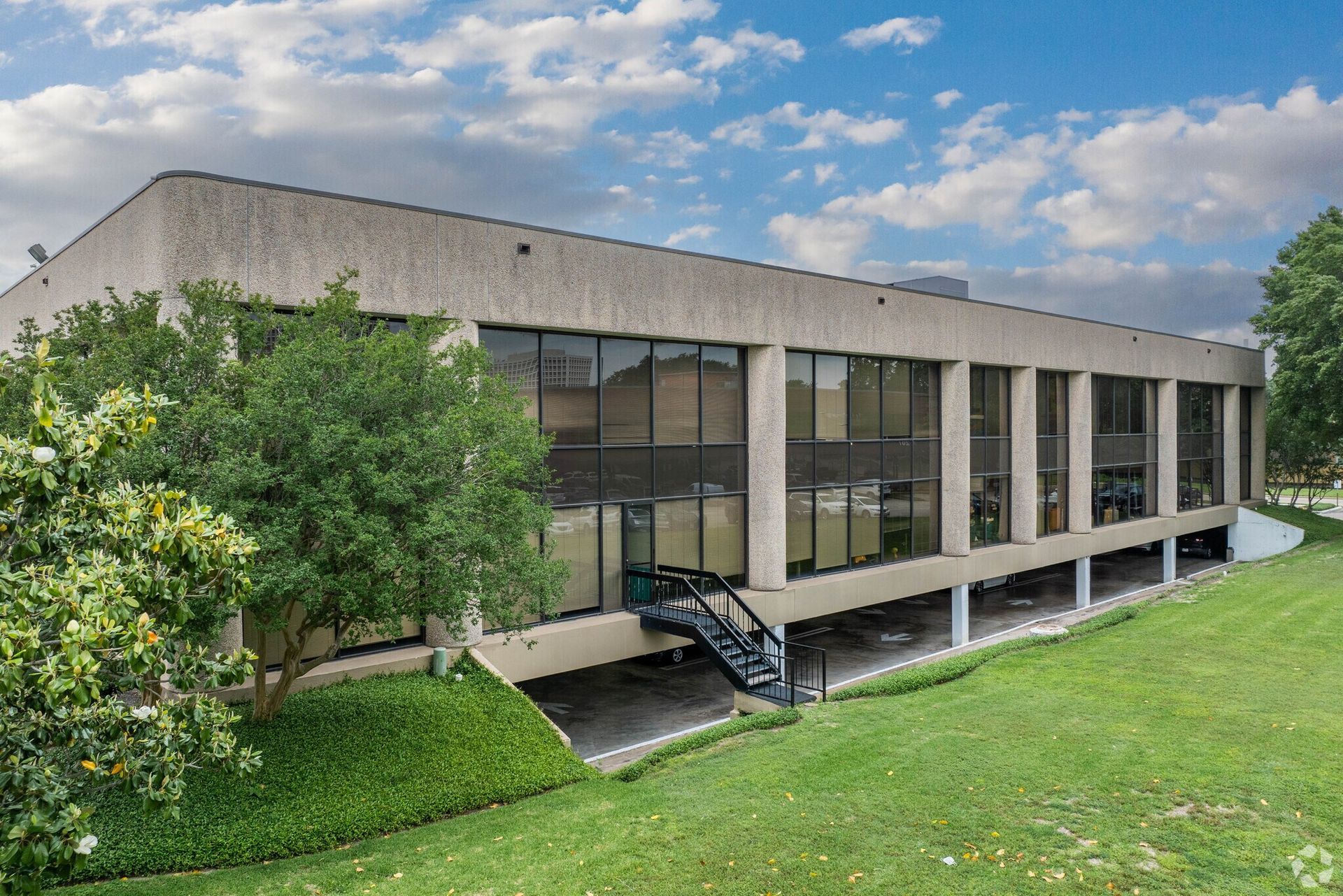Modern, two-story office building with reflective windows, lush landscaping, and signage in front.
