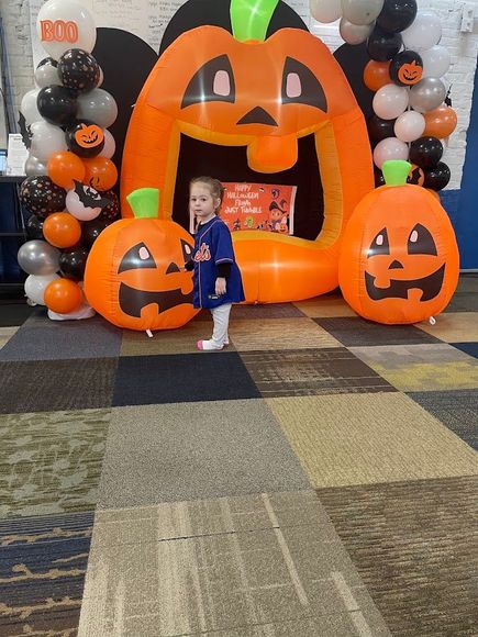 Child stands in front of inflatable pumpkins and balloon arch, Halloween decorations.