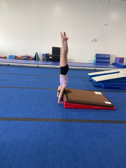 Gymnast doing a headstand on a mat in a gym.